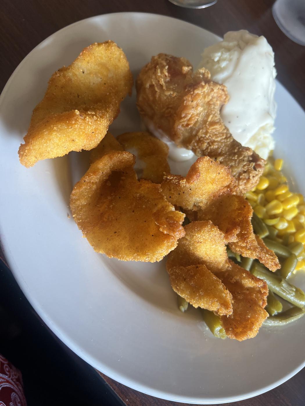 A buffet plate: cornmeal-fried fish, fried chicken, mashed potatoes under white gravy, sweetcorn and green beans.